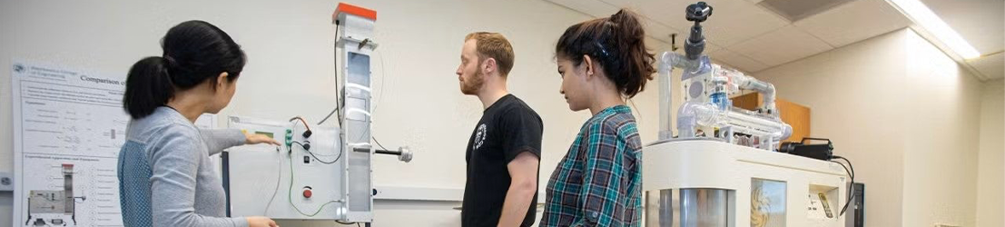 A professor showing and explaining lab equipment to two students in a classroom.