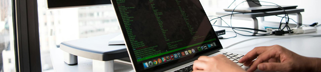 A person typing code on a laptop with two monitors.