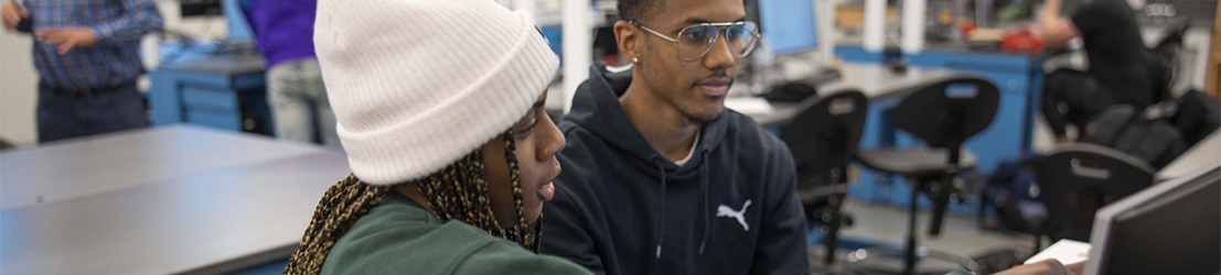 A female student pointing to a monitor to a male student. 