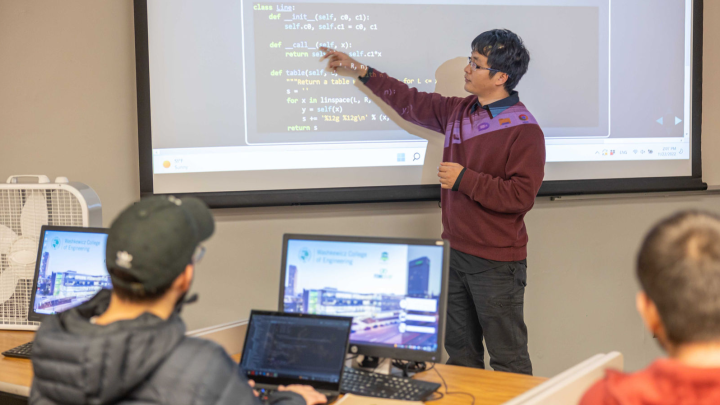A male professor teaching coding to a classroom full of students.