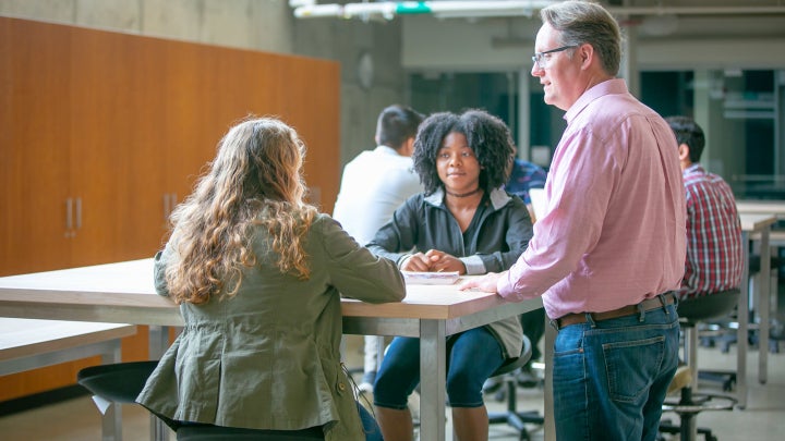 A male professor talking to two female students in a lab.