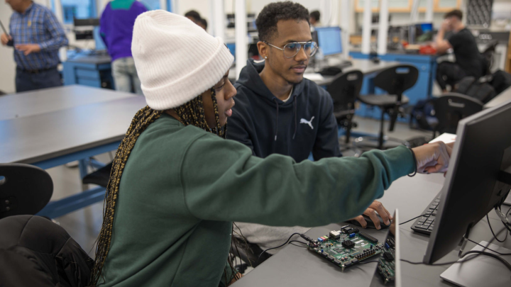 A female student pointing to a monitor to a male student. 