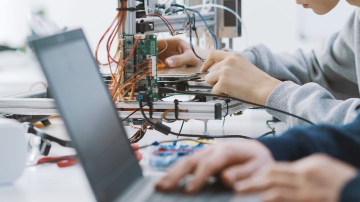 Two students working on a laptop and computer electronics in a classroom.