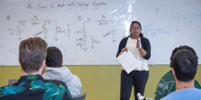 A professor teaching electrical engineering to a classroom full of students.