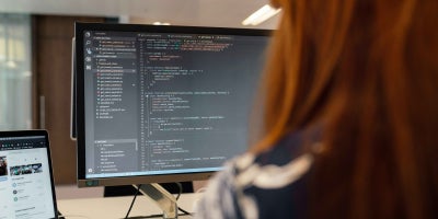 A female student working on code on a computer monitor.