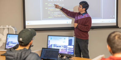 A male professor teaching coding to a classroom full of students.
