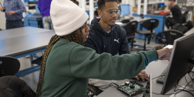 A female student pointing to a monitor to a male student. 