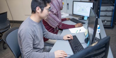 Two students working on computer desktops in a lab.