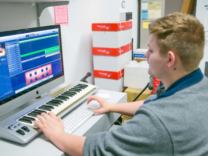 A male student mixing audio on a computer in a classroom.
