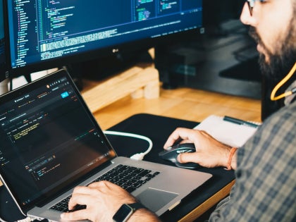 A male employee typing code on a laptop in a workplace.