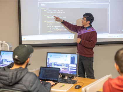 A male professor teaching coding to a classroom full of students.