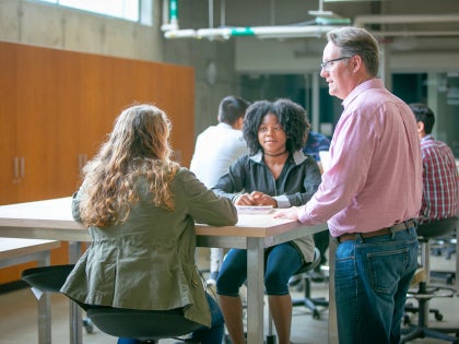 A male professor talking to two female students in a lab.