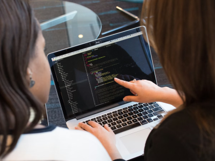 Two female students programming on a laptop.