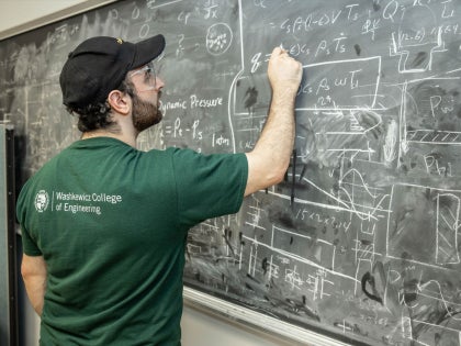 A student writing on a black chalkboard in a classroom.