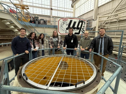 A group of students posing for a photo inside a large NASA facility.