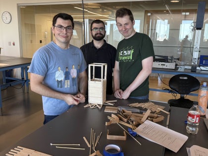 Three male students posing for a picture while working on a project in a classroom.