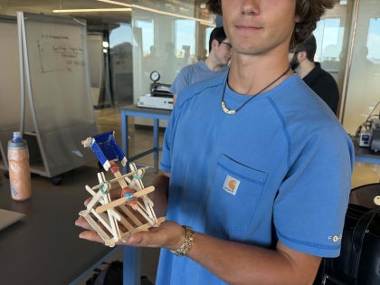 A male student holding a mechanical device inside a classroom.