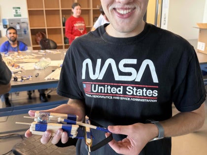 A male student holding a mechanical device in a classroom. 