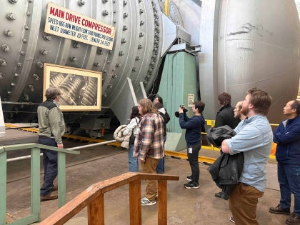 A group of students looking at a Main Drive Compressor inside a large facility.