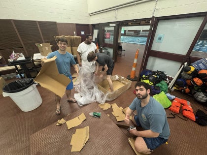 A group of students building a cardboard boat in a swimming facility.