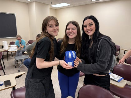 Three female students posing for a picture in a classroom. 