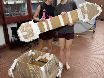 Two female students posing for a picture while holding a cardboard paddle.