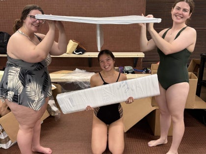 A group of students posing for a picture working on a cardboard boat.