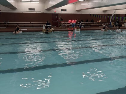 A wide shot of a swimming pool and a group of students in the background.