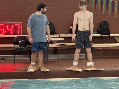 Two students with cardboard paddles in a swimming facility. 