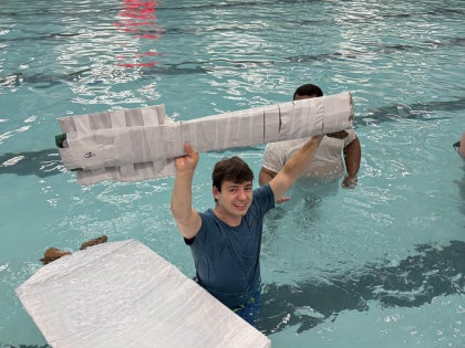 A male student holding a cardboard paddle inside a swimming facility.