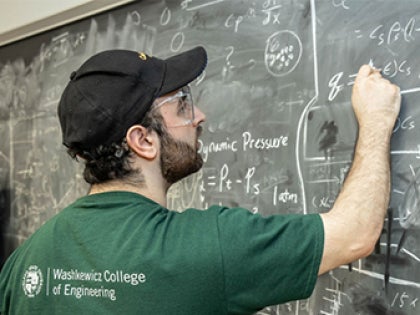 A student writing on a chalkboard in a classroom.